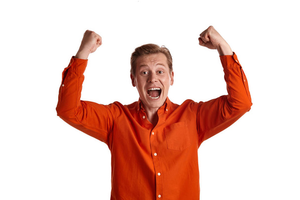Close-up portrait of a young excited ginger male in a stylish orange shirt acting like he is overjoyed about something while posing isolated on white studio background. Human facial expressions. Sincere emotions concept. Copy space. - Фото, изображение