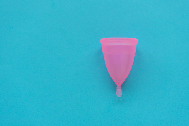 Copa menstrual rosa sobre fondo azul. Concepto de higiene íntima femenina. Vista superior
 - Foto, Imagen