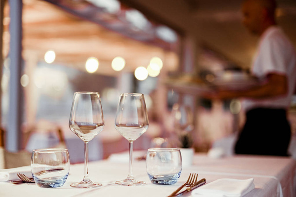 Ένα ποτήρι λευκό κρασί σε ένα τραπέζι σε ένα εστιατόριο. Ήπια φωτογραφία. Λάμψη και φως κηλίδες. Ελεύθερος χώρος για κείμενο. - Φωτογραφία, εικόνα