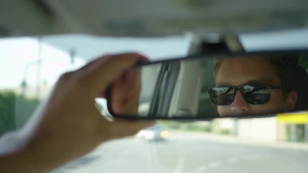 Zeitlupe, Nahaufnahme, dof: Junger Autofahrer stellt seinen Rückspiegel ein und sieht sich selbst beim Anhalten an einer roten Ampel an. schöner kaukasischer Mann checkt sich auf dem Weg zur Arbeit in der Stadt selbst aus - Filmmaterial, Video