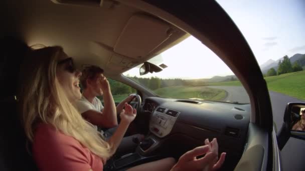 Slow Motion, Close Up: Neşeli çiftler kırsal yolda giderken arabalarında dans ediyorlar. Güneşli bir akşamda yolculuklarında eğlenen genç kadın ve erkeğin yavaş çekimleri.. - Video, Çekim