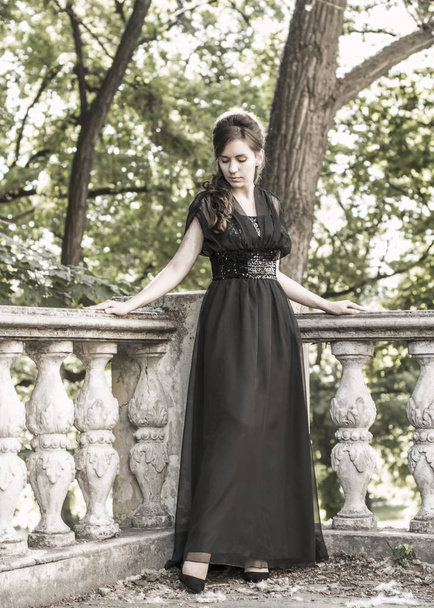 Piękna dziewczyna w czarnej wieczornej sukni w pobliżu klatki schodowej opuszczonego pałacu. Piękna kobieta z bliznów. Młoda dziewczyna w stylu retro. Ładna kobieta - Zdjęcie, obraz