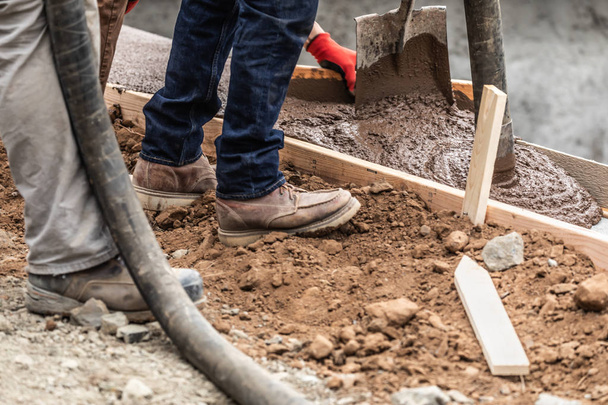 Trabalhadores da construção derramando e nivelando cimento molhado em moldura de madeira
 - Foto, Imagem