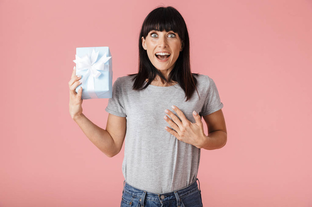 Beautiful amazing excited happy woman posing isolated over light pink background wall holding present gift box. - Foto, Imagen
