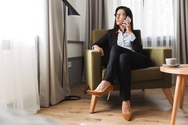 Beautiful serious young business woman in formal wear clothes indoors at home talking by mobile phone. - Foto, Bild