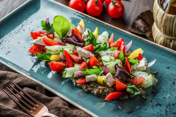 Греческий салат из органических овощей с помидорами, огурцами, оливками, сыром фета в тарелке на коричневом деревянном фоне. Здоровое питание, чистое питание, диета, вид сверху
 - Фото, изображение