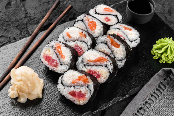 Sushi rolls and maki set with salmon and tuna fish, cheese and wasabi on black slate background. Japanese cuisine, close up - Photo, Image
