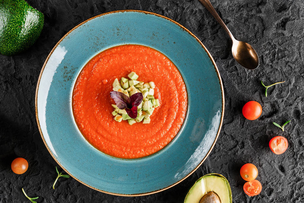 Gazpacho tomatensoep in bord met avocado en groente over donkere achtergrond. Gezond veganistisch eten, schoon eten, dieet, bovenaanzicht  - Foto, afbeelding