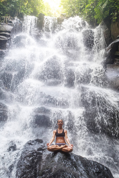 Woman practices yoga near waterfall in Bali, Indonesia - Фото, изображение