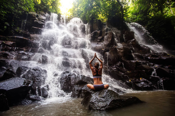 Woman practices yoga near waterfall in Bali, Indonesia - Foto, afbeelding