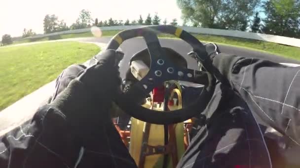 POV, LENS FLARE: Steering a speeding go cart along the winding asphalt circuit on a sunny day. Driving a fast cart in a black suit through sharp turns of a bumpy racetrack. Bright sun shines on racers - Footage, Video