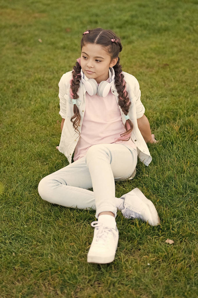 Sich selbst glücklich machen. Mädelsflechtfrisur und moderne Kopfhörer genießen Entspannung. Geheimnisse zur Erziehung glücklicher Kinder. Mädchen niedliches Kind grünes Gras Hintergrund. gesunde emotionale glückliche Kind entspannen im Freien - Foto, Bild