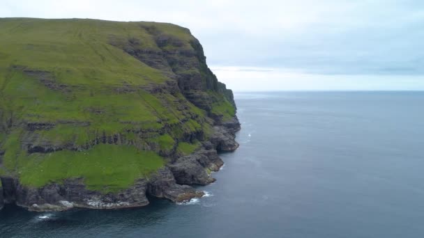 Aerial, Copy Space: repül végig egy lélegzetelállító füves sziklán, kilátással a nyugodt kék óceánra. Lenyűgöző felvétel a végtelen tengerről és a meredek zöld tájról a Feröer-szigetek érintetlen vidékén. - Felvétel, videó