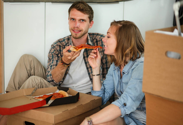 Young couple have a pizza lunch break on the floor after moving into a new home with boxes around them. Young couple - Foto, afbeelding