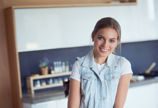 Portrait of young woman standing with arms crossed against kitchen background - Foto, afbeelding