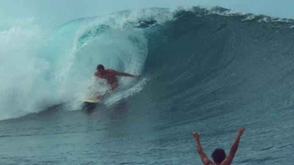 Slow Motion, Close Up: Onherkenbaar opgestookte surfer proost voor zijn vriend op een epische vatengolf in de buurt van populaire surfspot. Surfboarder geeft de shaka aan een vriend die een adembenemende buizengolf vangt. - Video