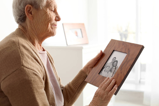 Elderly woman with framed family portrait at home - Φωτογραφία, εικόνα