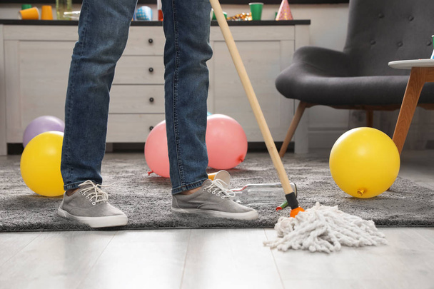 Man met MOP schoonmaken rommelig kamer na feestje, close-up van benen - Foto, afbeelding