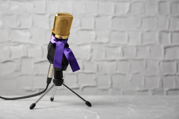 Microphone with purple awareness ribbon on table against white wall, space for text - Fotó, kép