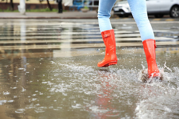 Woman with red rubber boots running in puddle, closeup. Rainy weather - Фото, зображення