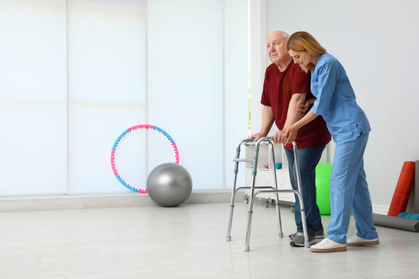 Caretaker helping elderly man with walking frame indoors - Foto, Bild