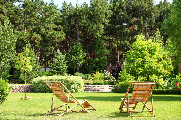 Wooden deck chairs in beautiful garden on sunny day - Фото, изображение