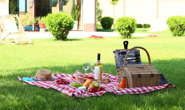 Picnic basket with products and bottle of wine on checkered blanket in garden. Space for text - Foto, immagini