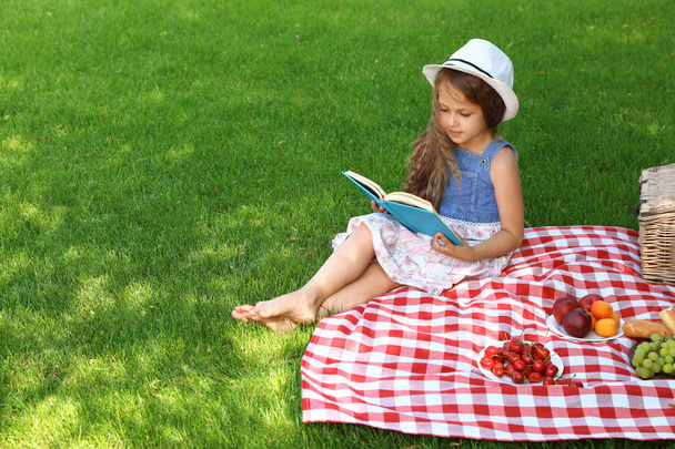 Cute little girl reading book outdoors. Summertime rest - 写真・画像