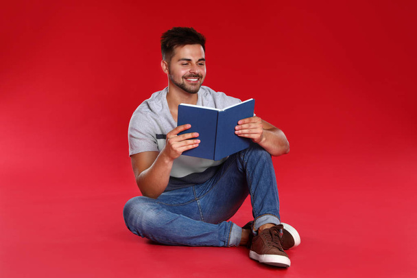 Handsome young man reading book on red background - Fotó, kép