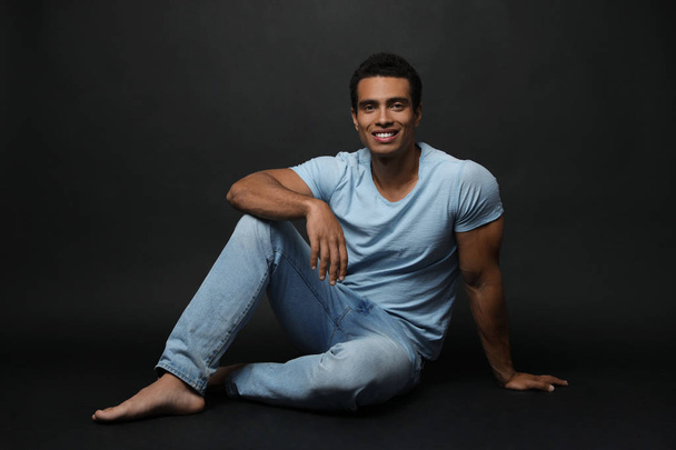 Handsome young African-American man sitting on black background - Foto, Bild