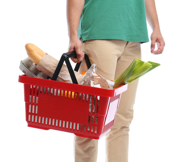 Young man with shopping basket full of products isolated on white, closeup - Valokuva, kuva