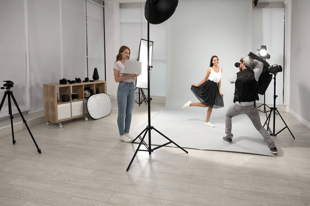 Professional photographer with assistant taking picture of young woman in modern studio - 写真・画像
