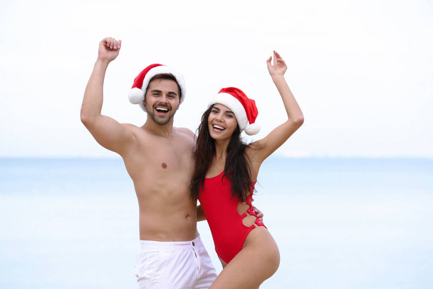 Happy young couple with Santa hats together on beach - Фото, изображение