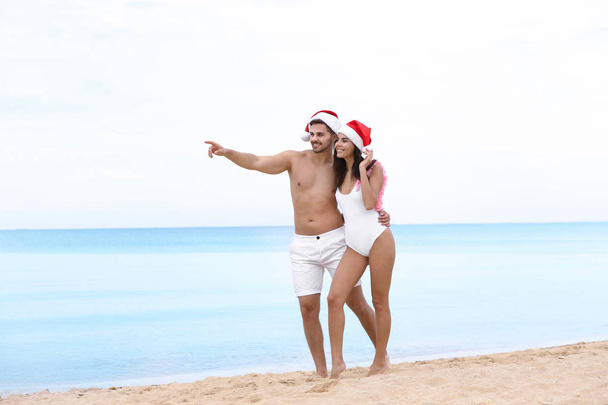 Happy young couple with Santa hats on beach near sea - Φωτογραφία, εικόνα