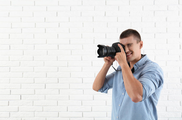 Young professional photographer taking picture near brick wall. Space for text - Foto, Bild