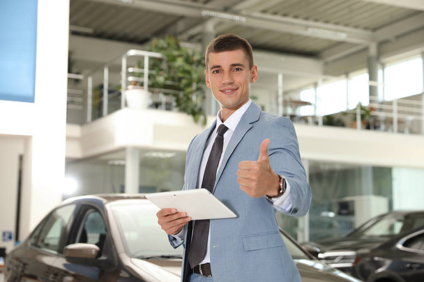 Young salesman with tablet in modern car dealership - Foto, Imagen