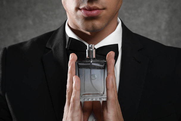Handsome young man with bottle of perfume on grey stone background, closeup - Фото, зображення
