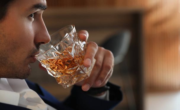 Young man with glass of whiskey indoors, closeup - Фото, изображение