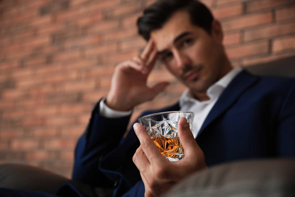 Young man with glass of whiskey near brick wall indoors - Valokuva, kuva