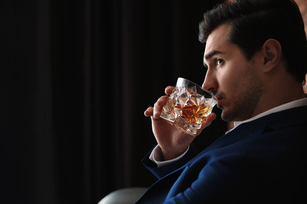 Young man with glass of whiskey indoors. Space for text - Foto, afbeelding