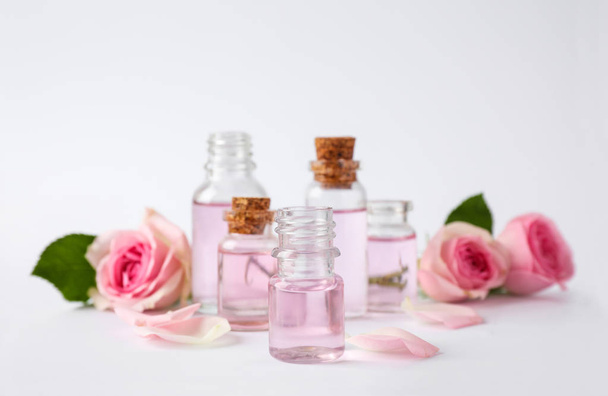 Bottles of essential oil and roses on white background - Photo, Image