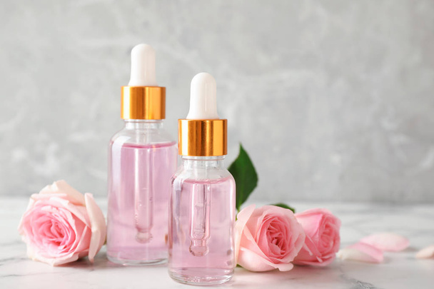Bottles of essential oil and roses on marble table - Fotó, kép