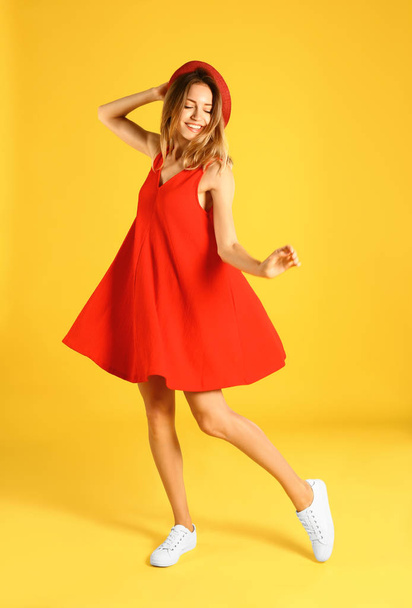 Beautiful young woman in red dress dancing on yellow background - Фото, зображення