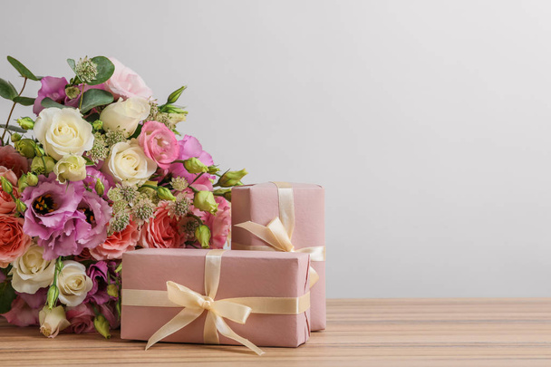 Beautiful bouquet of flowers and gift boxes on wooden table against light background. Space for text - Zdjęcie, obraz