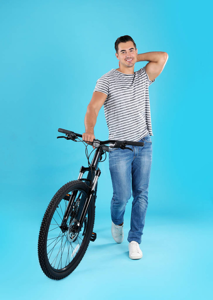 Handsome young man with modern bicycle on light blue background - Zdjęcie, obraz