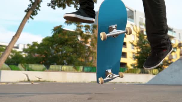 Zeitlupe, Nahaufnahme: Junge männliche Skateboarder landen an einem sonnigen Tag im Skatepark einen variablen Kickflip. Filmaufnahme eines unkenntlich gemachten männlichen Athleten bei einem coolen Stunt mit seinem blauen Skateboard. - Filmmaterial, Video