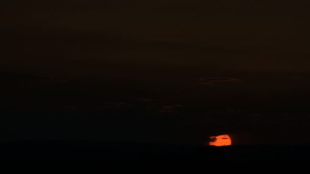 Timelapse van de ondergaande zon bij zonsondergang over een klein stadje. Low Key - Video