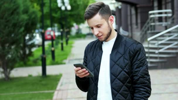Knappe bebaarde man gebruikt de telefoon op straat in, tekst typen, chatten - Video