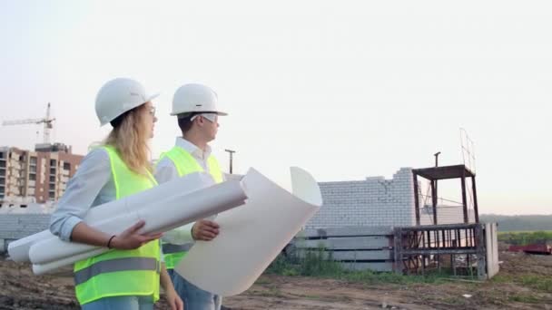The builder and architect man and woman are discussing the construction plan of the modern business center standing near construction site. They go to the building - Footage, Video