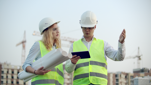 Two industrial engineer wear safety helmet and holding tablet engineering working and talking with drawings inspection. On building outside. Engineering tools - Footage, Video